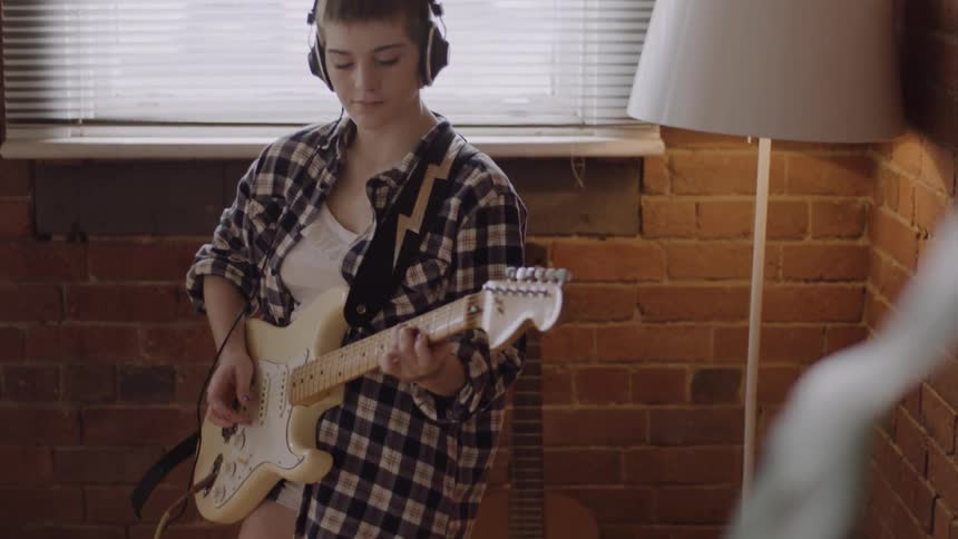 A woman wearing earphones places the guitar
