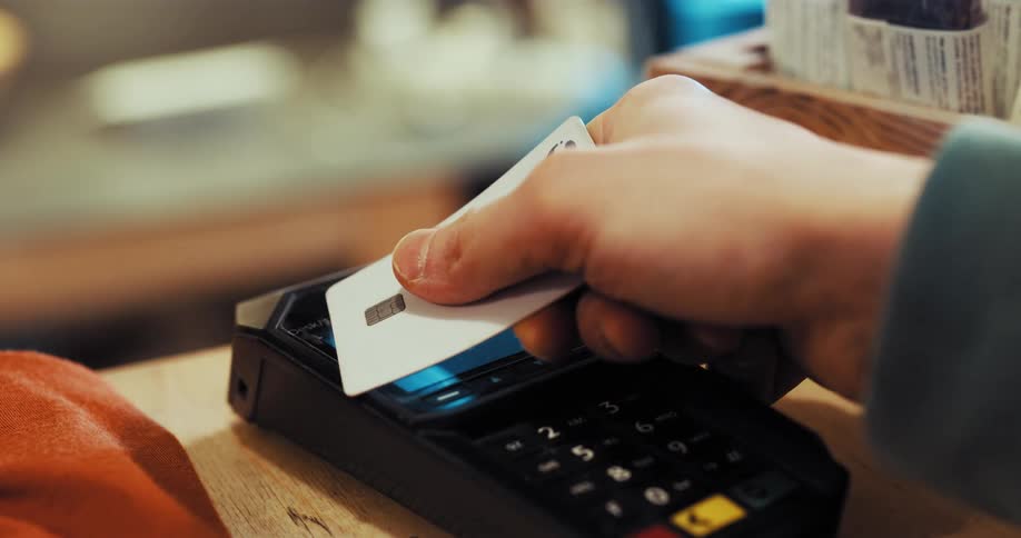 A person is holding a credit card in their hand as they move it over a credit card payment machine