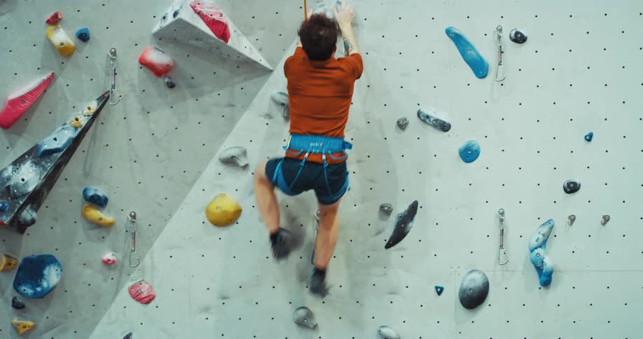 A man climbing a rock wall reaching the top and then dropping and celebrating while swinging