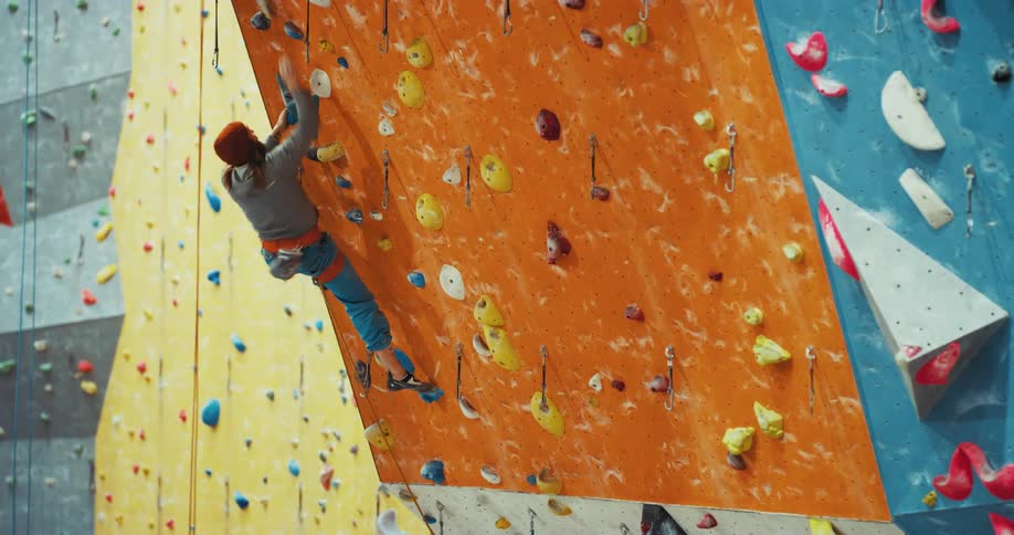 Man with red hat gray hoodie an jeans climbs outdoor climbing wall