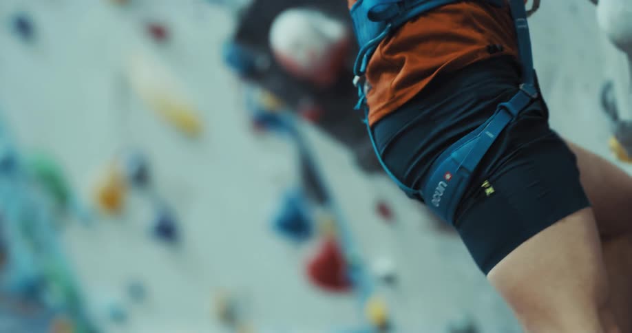 Man wearing harness climbs wall in climbing gym