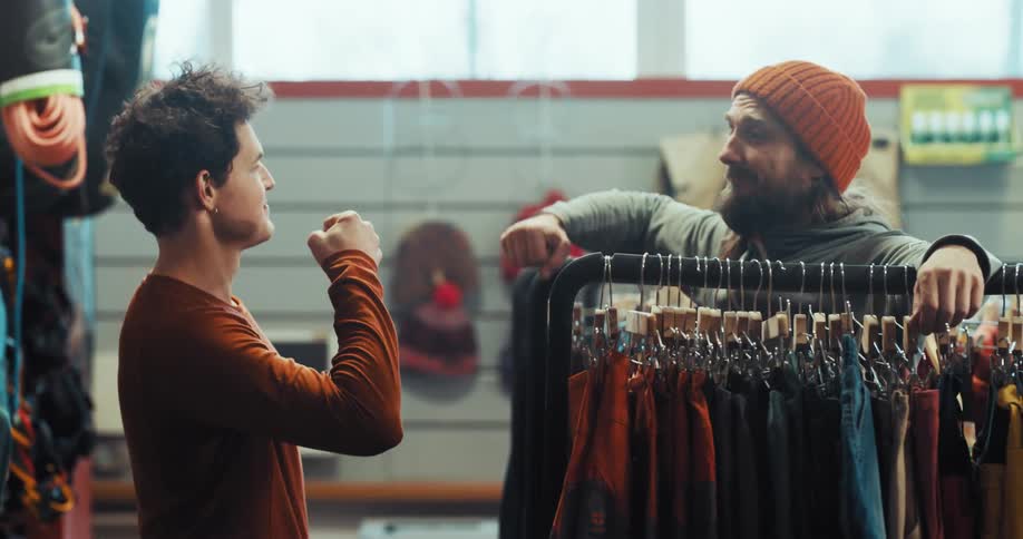 A man tries on a shirt and gets a thumbs up from a friend