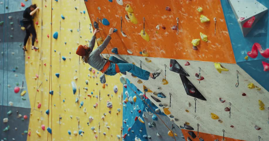 While woman climbing down man climbing up outdoor climbing wall
