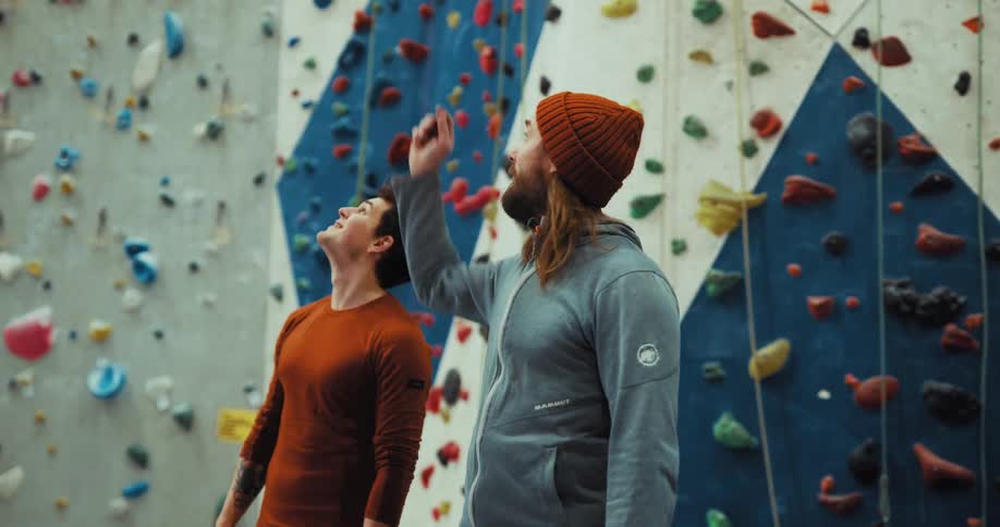 Two men greeting each other talking and looking around at a room with arock climbing wall in it