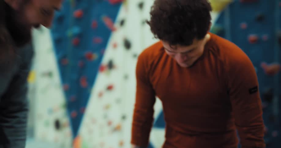 Two men happily hug and then talk while at an indoor climbing gym