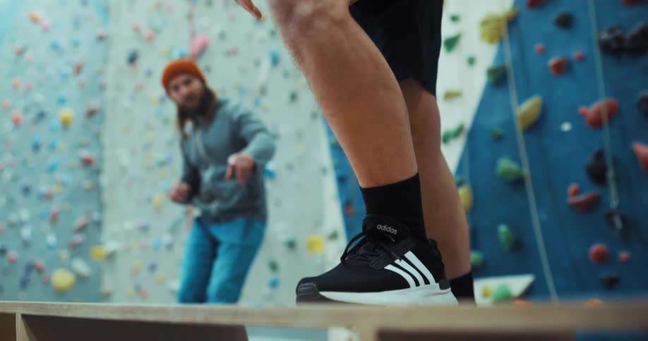 An up close of a mans calf and sneaker while another man guides him and talks to him