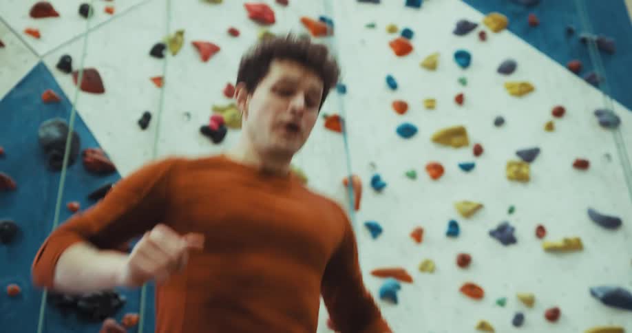 A man shows another man a jumping exercise in front of an indoor climbing wall