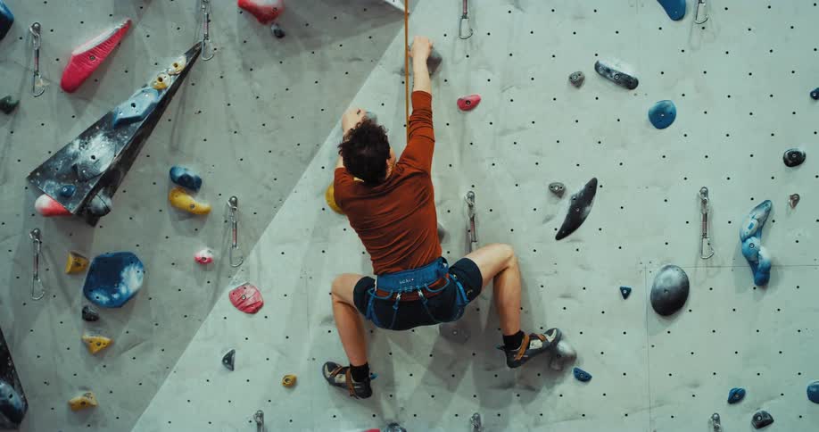 A man climbing a rock wall and then letting go and swinging clapping his hands