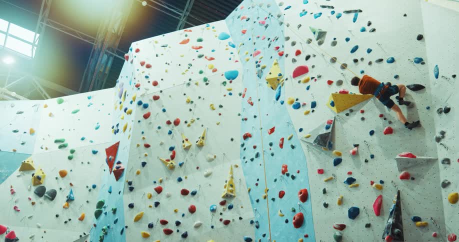 A man is scaling a climbing wall as he slips and looks down as he climbs