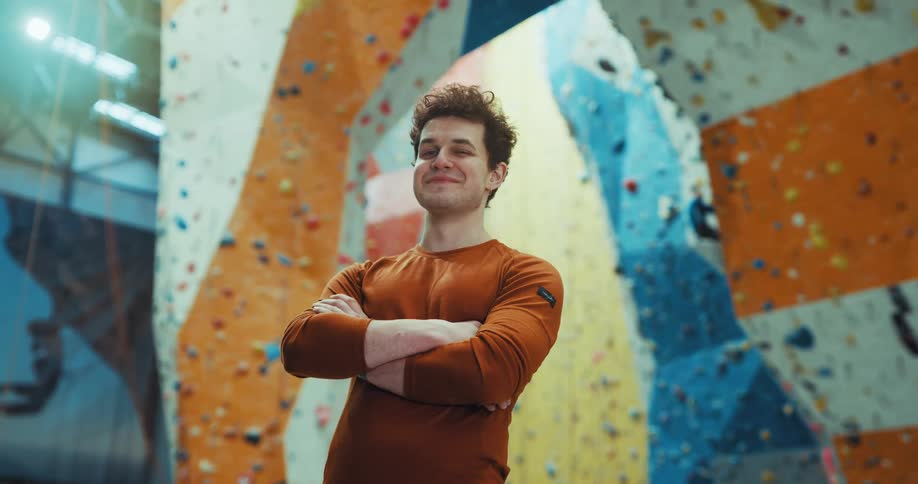 A man smiles while standing in front of an indoor rock climbing wall