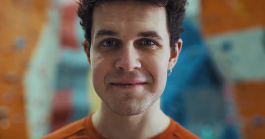 Man with orange shirt smiles at camera in front of climbing wall