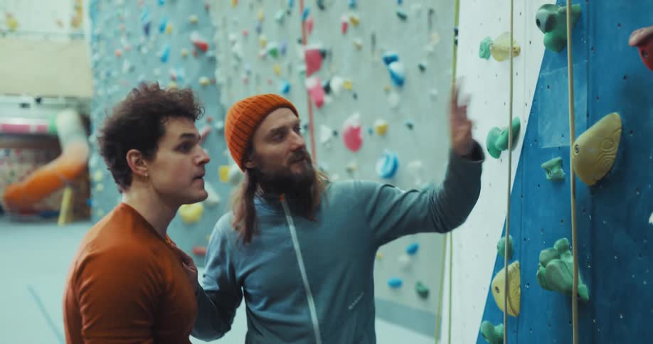 A man slips while climbing a rock wall and receives instruction from another man