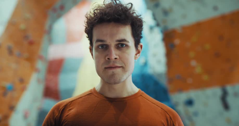A man is standing near a climbing wall and he takes a breath as he looks up and smiles