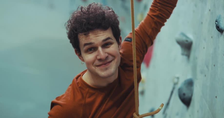 A rock wall climber looks up and then smiles at the camera