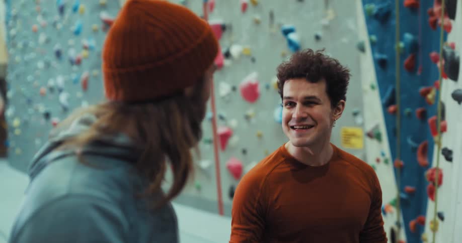 A man looking up smiling as another man comes over to greet him and smiles and laughs with him