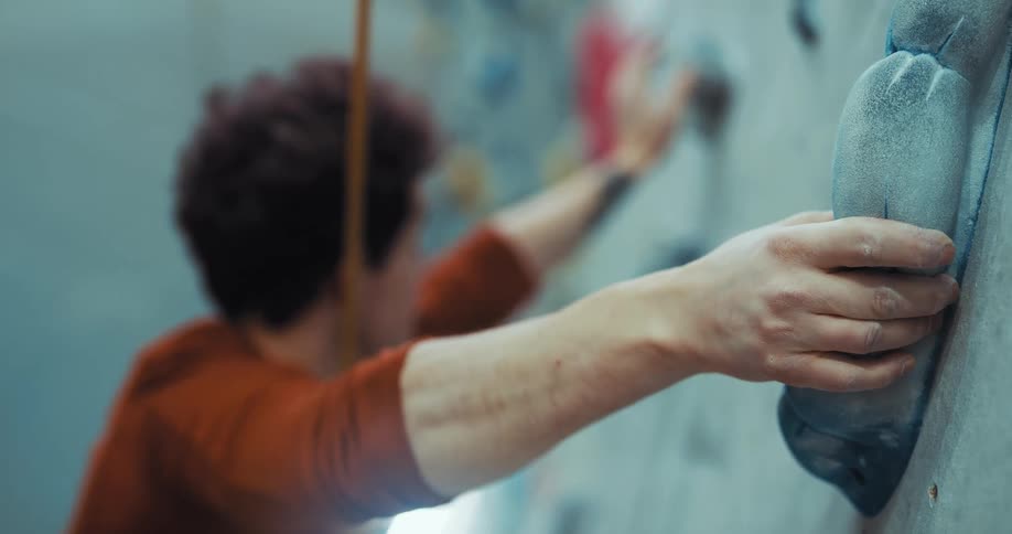A man gripping a rock on a rock climbing wall and looking where to grab next