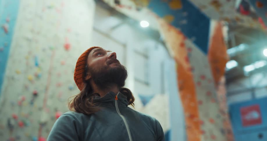 A man wearing an orange beanie looking upward holding a rope and talking