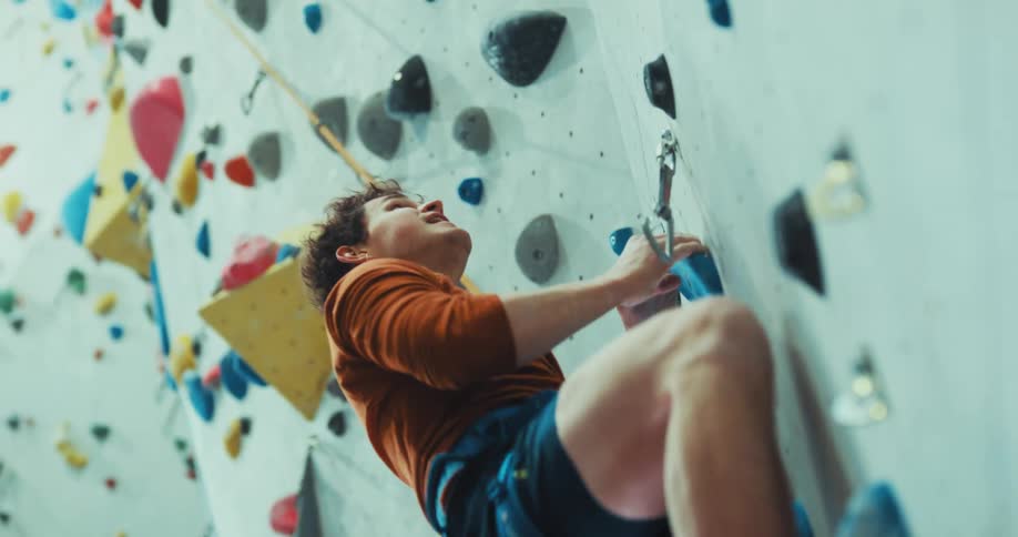 A man slowly climbs an indoor climbing wall