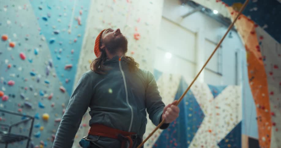 A man checks the rope while monitoring someone on a rock climbing wall