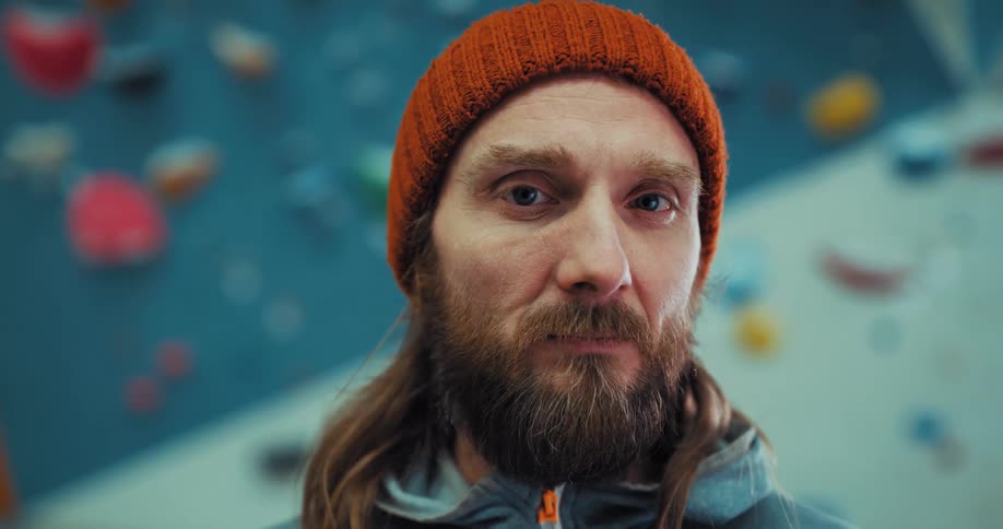 A man smiles while standing in front of an indoor rock climbing wall