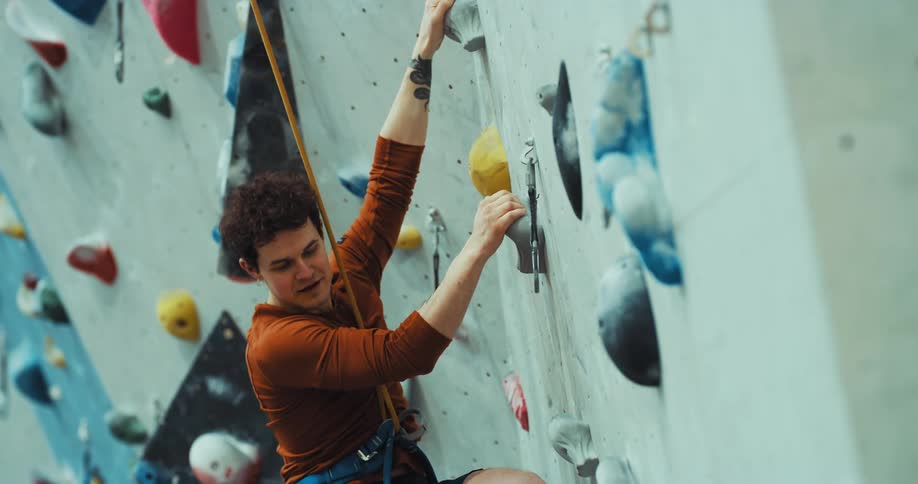 A man has a harness and rope around his waist as he scales a climbing wall