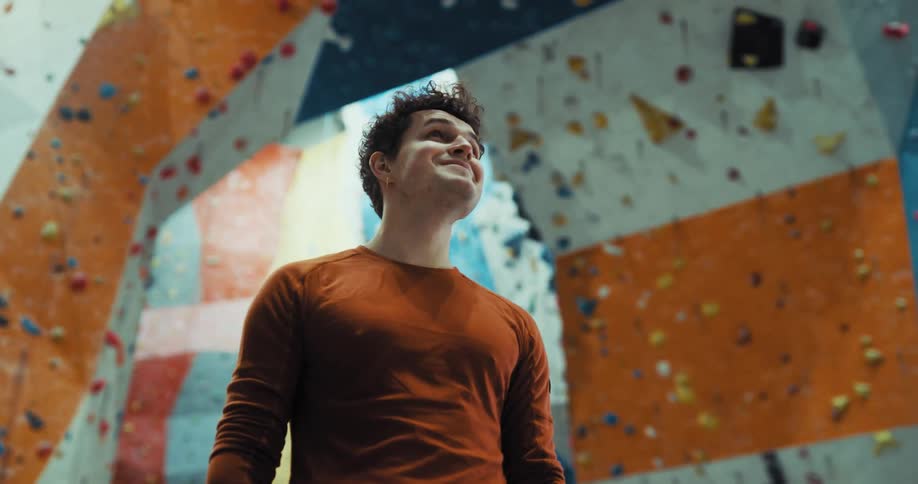A man is standing near climbing walls smiling as he looks around