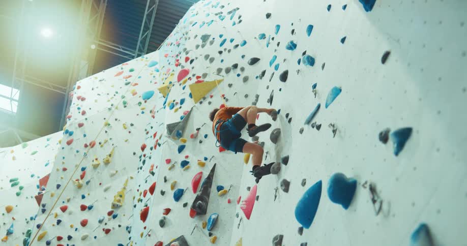 A man is climbing up the wall in the gym