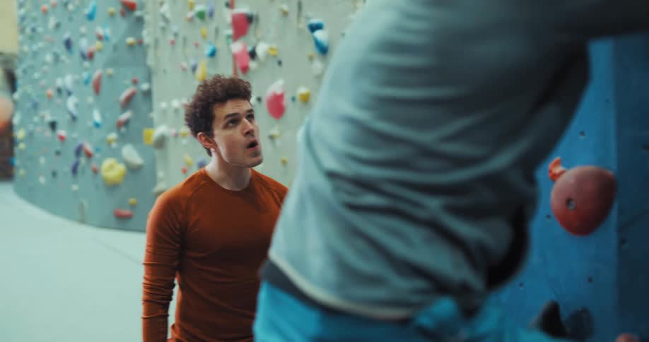 Man demonstrates climbing on wall to another at climbing gym