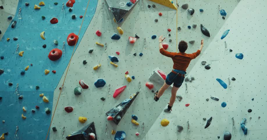 A man has a harness and rope around his waist and slips scaling a wall as he swings and from his rope