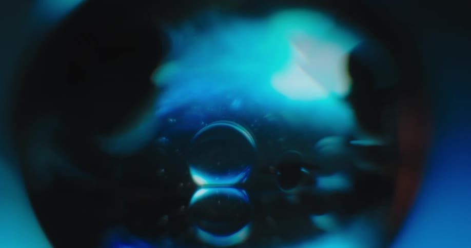 Blue light in the distance reflects inside a crystal ball and the reflection shines on a mirrored surface in the darkness
