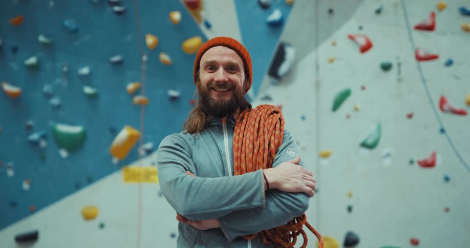 A rock climber smiles while posing in front of an indoor rock wall