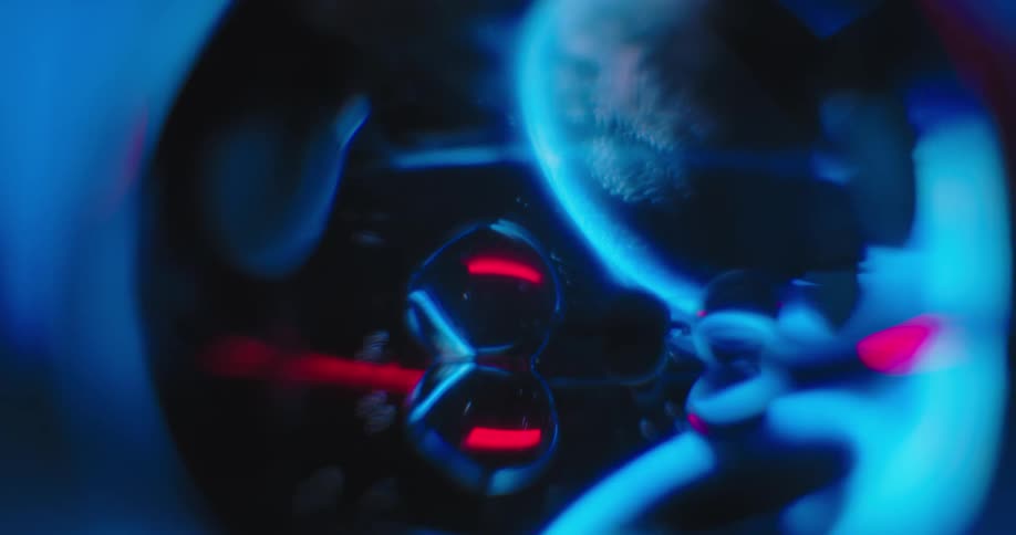 Blue and red light reflects on orbs as a globe moves across the darkness