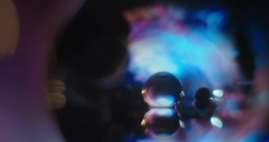 Blue and purple light glows in the distance as the reflection of clear orbs shine in other clear orbs