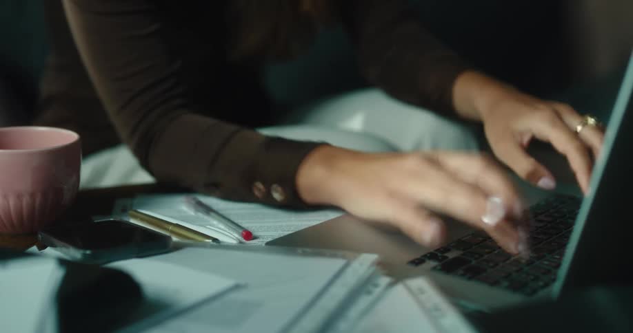 Woman sits working on laptop computer and doing paperwork