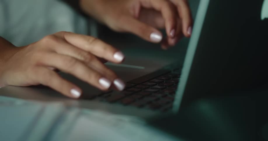 A close up of a womans fingers typing on a laptop keyboard