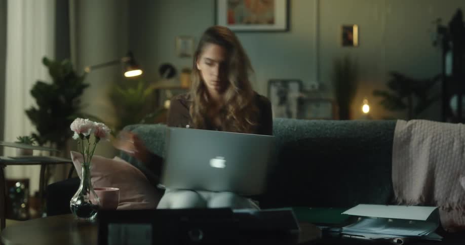 A woman is sitting at a table with a laptop computer as she goes though folders and paperwork