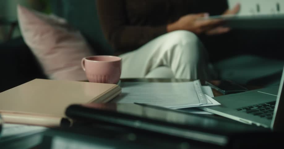 A woman shuffling papers on a coffee table writing and closing her laptop cleaning off the table