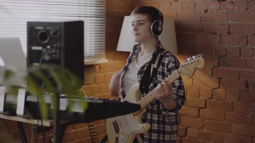 A woman wearing headphones plays an electric guitar