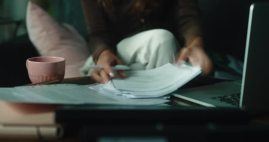 A woman is sitting at a table with a laptop computer and doing paperwork as she drinks coffee and closes her laptop when she is all done