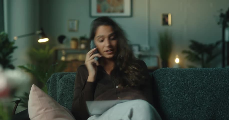 A woman sitting on her couch talking on the phone laughing and smiling