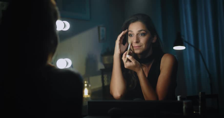 A woman puts on makeup while sitting at her vanity table