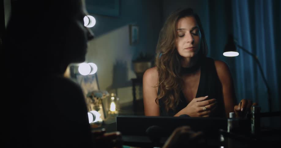 A woman applying eye makeup in a mirror checking it and smiling