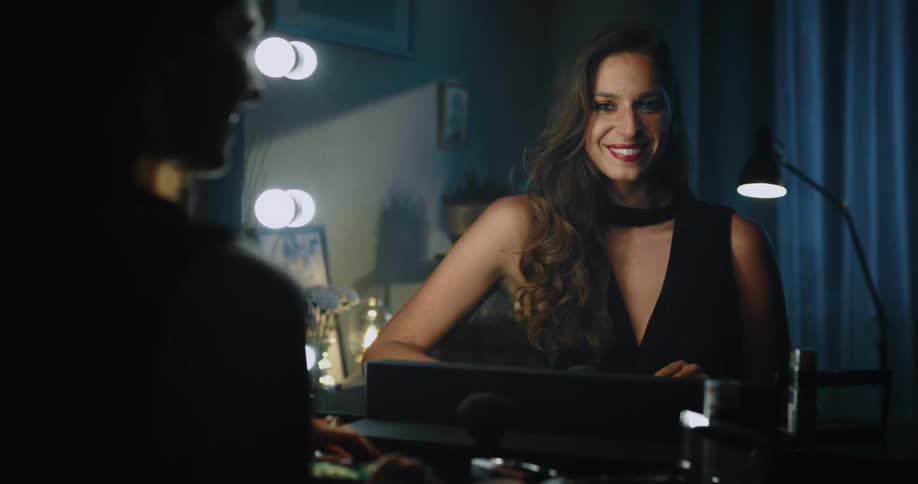 A woman is sitting in front of a mirror smiling as she looks at herself