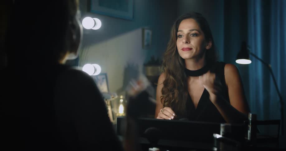 Woman wearing evening dress applies lipstick then smiles at her reflection