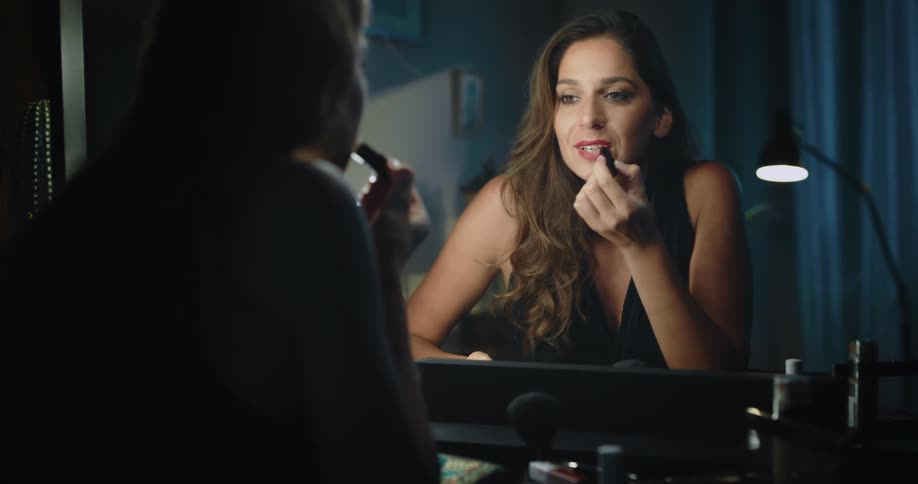 Woman sits and gets ready by applying lipstick and checking her hair