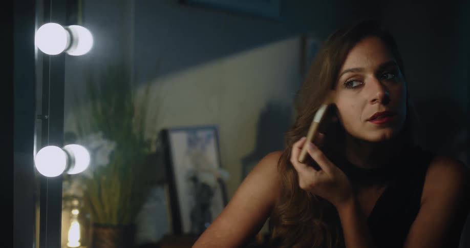Woman with brown hair applying makeup to the face looking in mirror
