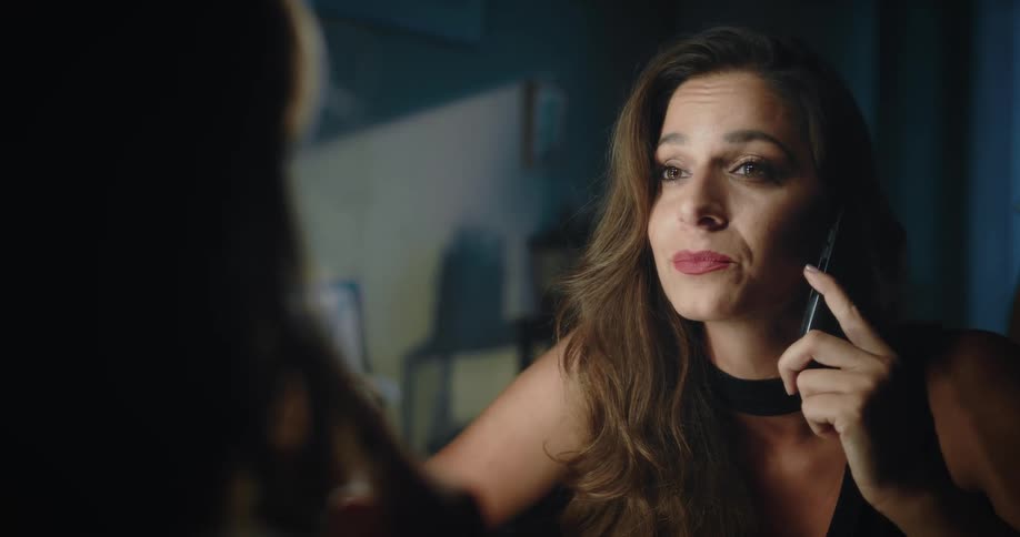 A womans reflection in a mirror as she smiles and laughs talking on her cell phone