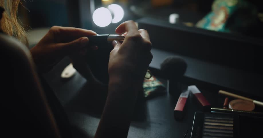 A woman removes cosmetics from a makeup bag and opens a tube of lipstick