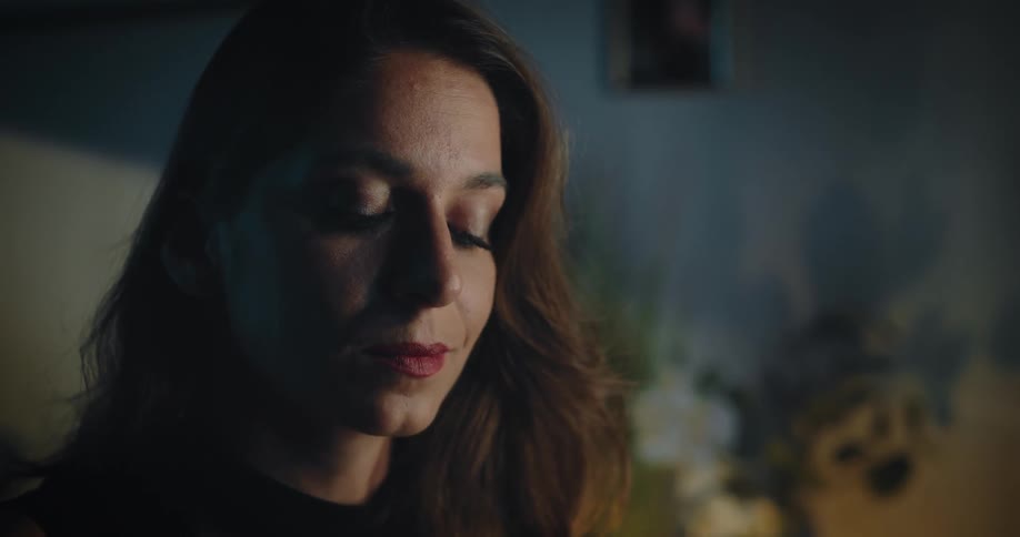 A woman is sitting in front of a mirror looking at her face as she puts makeup on her eyelids