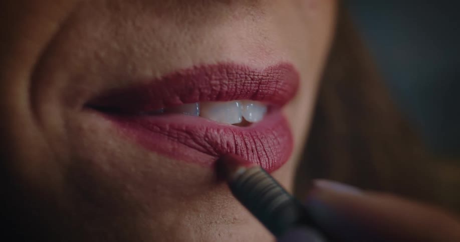 An extreme close up of a woman putting lipstick on her lips